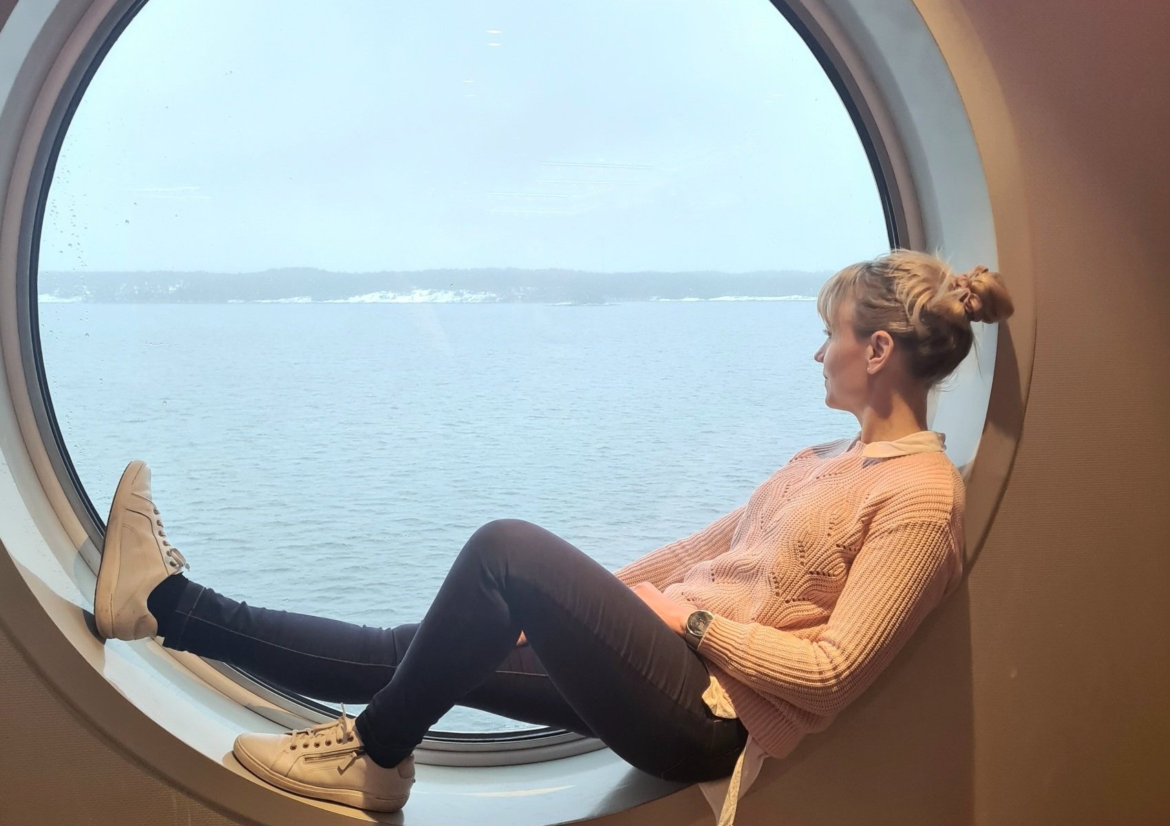 nainen istuu laivan pyorealla ikkunalla ja katsoo merelle