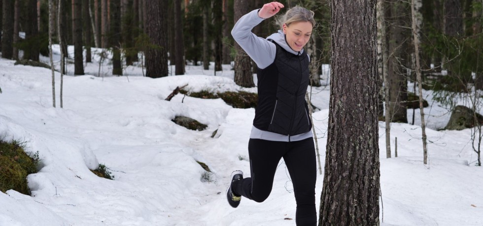 nainen juoksee lumisessa metsassa